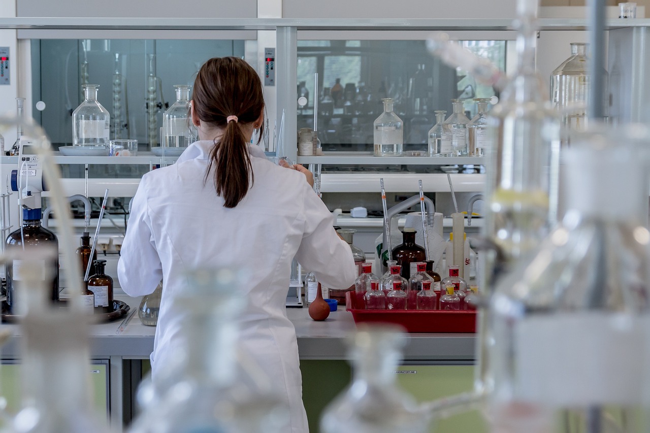 Person with pony tail in hair working at a lab station in a white coat