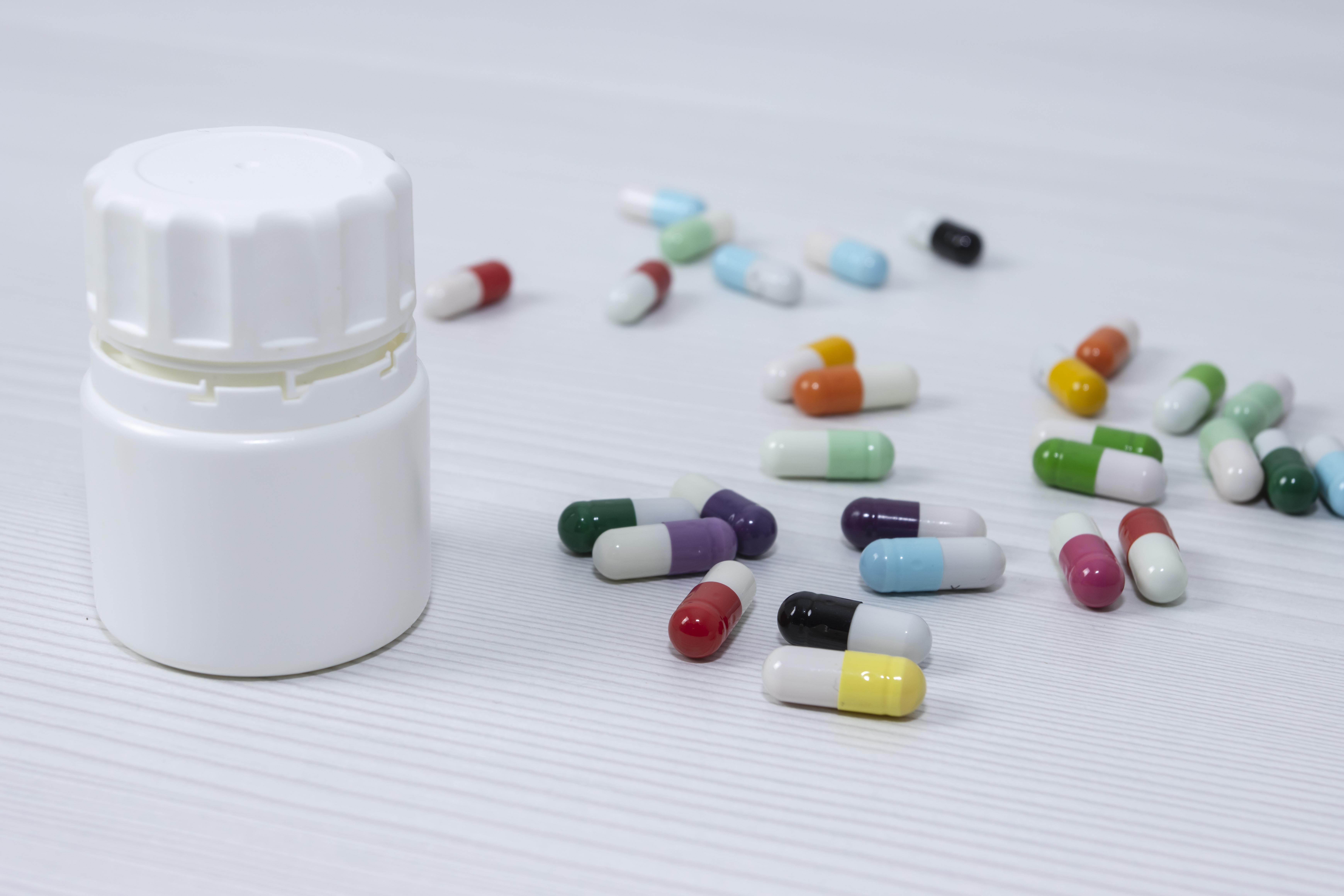 colored pills and a pill bottle on a white surface