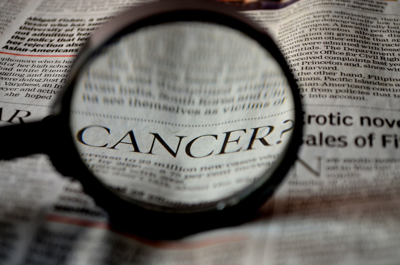 magnifying glass over word CANCER in newspaper
